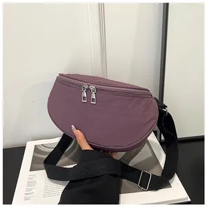 Detail of deep purple nylon crescent bag with silver zippers on a minimalist backdrop
