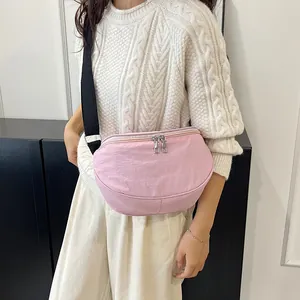Pink crescent saddle bag with black adjustable strap worn by a model in casual knitwear