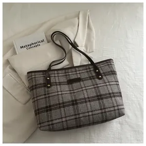 Close-up of grey plaid wool tote bag with slim brown handles and gold metal rivets