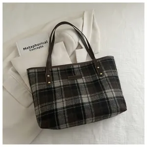Close-up of vintage plaid wool tote bag with brown leather details on a white suit