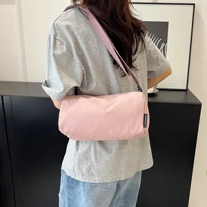 Pink nylon barrel crossbody bag with adjustable strap worn by model in minimalist indoor setting