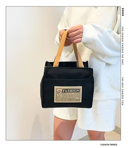 Détail du sac cabas en toile noire montrant des poignées tissées et une poche avant