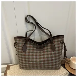 Detailed view of gray-green plaid tote bag with brown leather handles and metal rivets