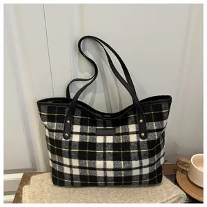 Detail of checkered woolen tote bag with leather straps and gold rivets in cozy setting