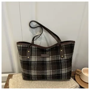 Detail of plaid tote bag featuring brown leather straps and gold metal rivet accents