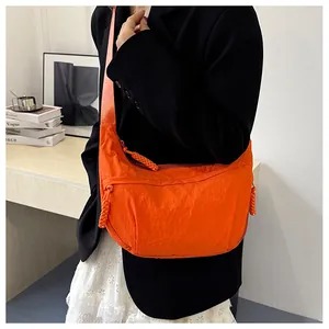 Macro view of a vibrant orange nylon crescent bag worn by a model in a casual setting