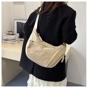 Detail of a beige nylon crescent crossbody bag with a thick woven rope zipper pull