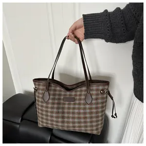 Detail of plaid fabric texture and brown leather strap on a large shoulder tote bag