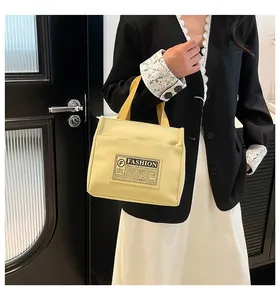 Détail du sac cabas en toile jaune avec étiquette mode sur blazer noir et robe blanche
