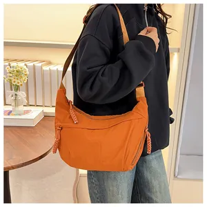 Detail of adjustable strap and orange nylon crescent bag shown in a cozy indoor setting