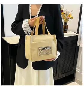 Détail du sac cabas en toile montrant le corps crème, les anses jaunes et l'étiquette
