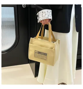 Détail du sac cabas en toile beige avec étiquette mode et poche avant tenu par un modèle