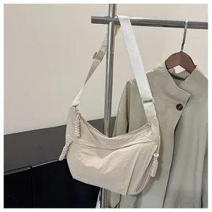 Detail of beige nylon crescent crossbody bag featuring adjustable strap and cord zipper pull