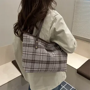 Large checkered tote bag with brown leather handles worn by a model in a minimalist room