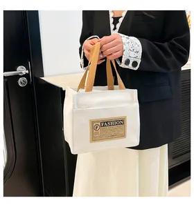 Détail d'un petit sac en toile blanc avec anses marron et écusson en cuir tendance