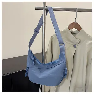 Detail view of smog blue nylon crescent bag on hanger paired with beige trench coat