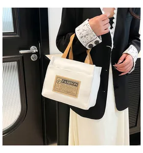 Détail d'un sac cabas en toile blanche avec anses marron et étiquette fashion brodée