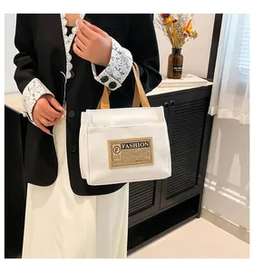 Détail d'un sac cabas en toile blanche avec des anses marron et une poche zippée devant
