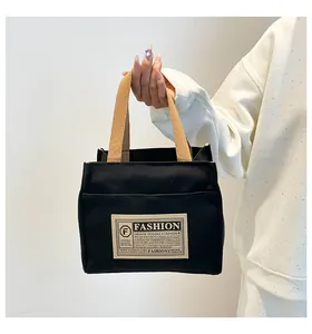 Détail d'un sac cabas en toile noire avec anses brunes et une poche avant élégante