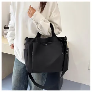 Détail d'un grand sac cabas noir avec bandoulière réglable et poche à bouton-pression métal