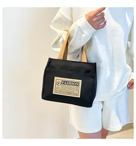 Détail d'un sac cabas en toile noire avec des poignées kaki et une étiquette minimaliste