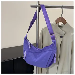 Detail of a purple nylon crescent bag with adjustable strap shown against a beige coat