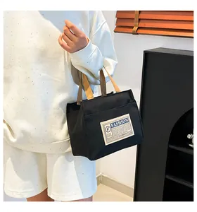 Détail du sac en toile noire avec étiquette fashion blanche et poignées marron