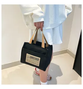 Détail d'un sac cabas en toile noire avec anses beiges et écusson de mode porté
