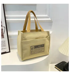 Détail du sac cabas en toile beige avec poignées jaunes et un écusson décoratif tendance