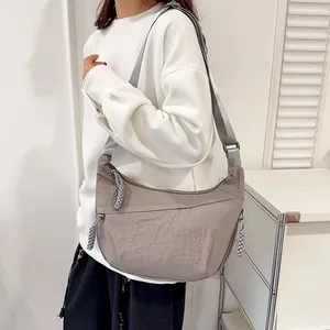 Minimalist taupe nylon crescent crossbody bag with thick shoulder strap shown on model