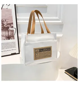 Détail du sac cabas en toile blanche avec poignées en tissu marron et écusson de mode