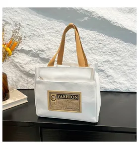 Détail d'un sac fourre-tout en toile blanche avec anses marron et étiquette en cuir