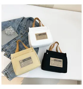 Trois sacs cabas en toile blanc, beige et noir avec des anses marron dans une mise en scène
