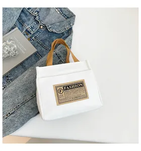 Détail du sac cabas en toile blanche avec poignées tissées brunes et étiquette vintage