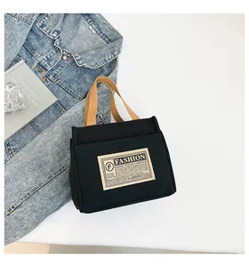 Détail du sac cabas en toile noire avec étiquette de mode et anses marron sur table
