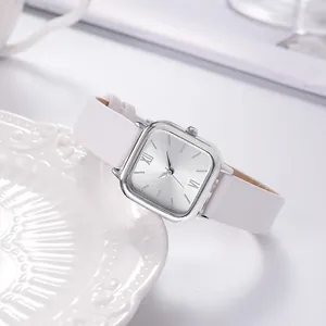 Detail of square silver quartz watch with white leather strap on a ceramic plate