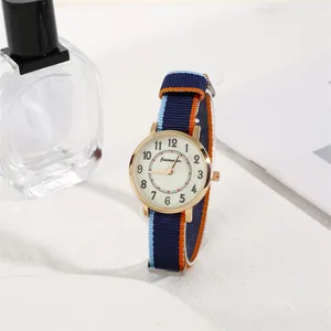 Detail of round gold quartz watch with tri-color nylon strap on a white sandy display