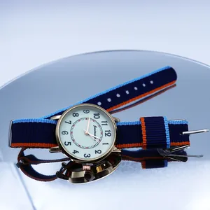 Close-up of golden quartz watch with tri-color striped nylon strap on reflective surface