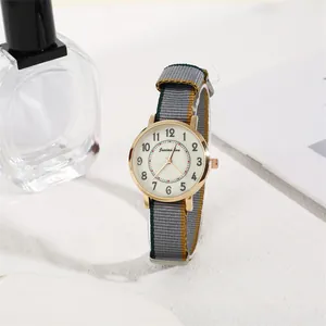 Detail of a gold case watch with a tricolor nylon strap next to a perfume bottle