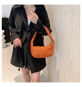 Sac à main matelassé orange à texture florale porté avec un manteau noir élégant