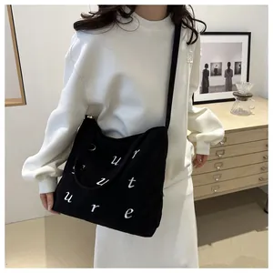 Borsa tote in velluto a coste nero con lettere ricamate bianche indossata da una modella