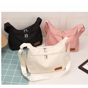 Three multi-pocket nylon crossbody bags in black, pink and beige shown on a table