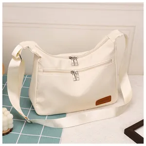Detail of cream nylon crossbody bag with dual front zippers and fashion leather patch