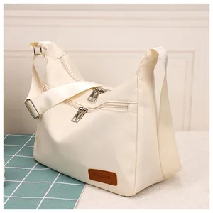 Detail of off-white waterproof crossbody bag with dual zipper pockets and leather patch
