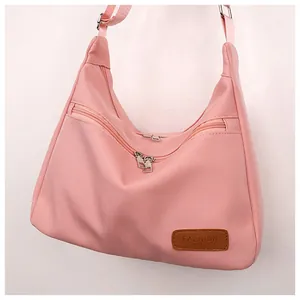 Detailed view of pink nylon crossbody bag with three metal zippers and leather label