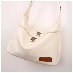 Detail of off-white crossbody bag with silver zippers and brown fashion leather patch