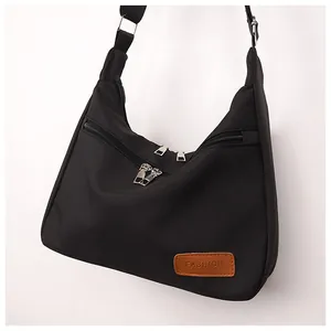 Detail of black nylon crossbody bag featuring dual silver zippers and a brown leather tag