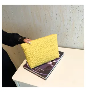 Detail of yellow quilted clutch featuring embossed floral texture held by a hand