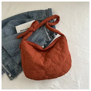 Detail of caramel heart quilted nylon bag featuring a wide knotted shoulder strap