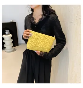Detail of bright yellow quilted envelope clutch with 3D floral texture held by model